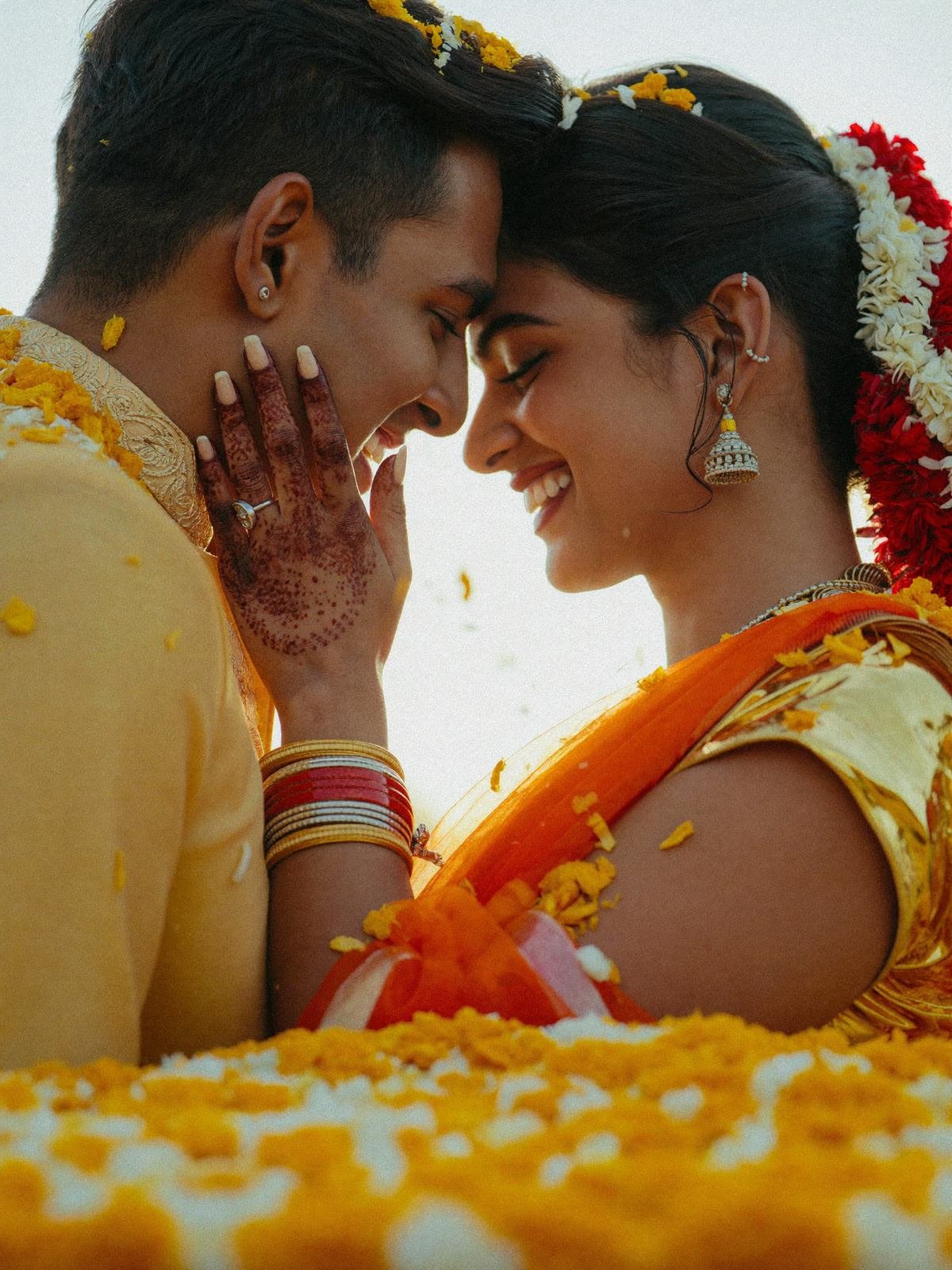 Couple foreheads together in a shower of marigold petals during haldi, golden backlight